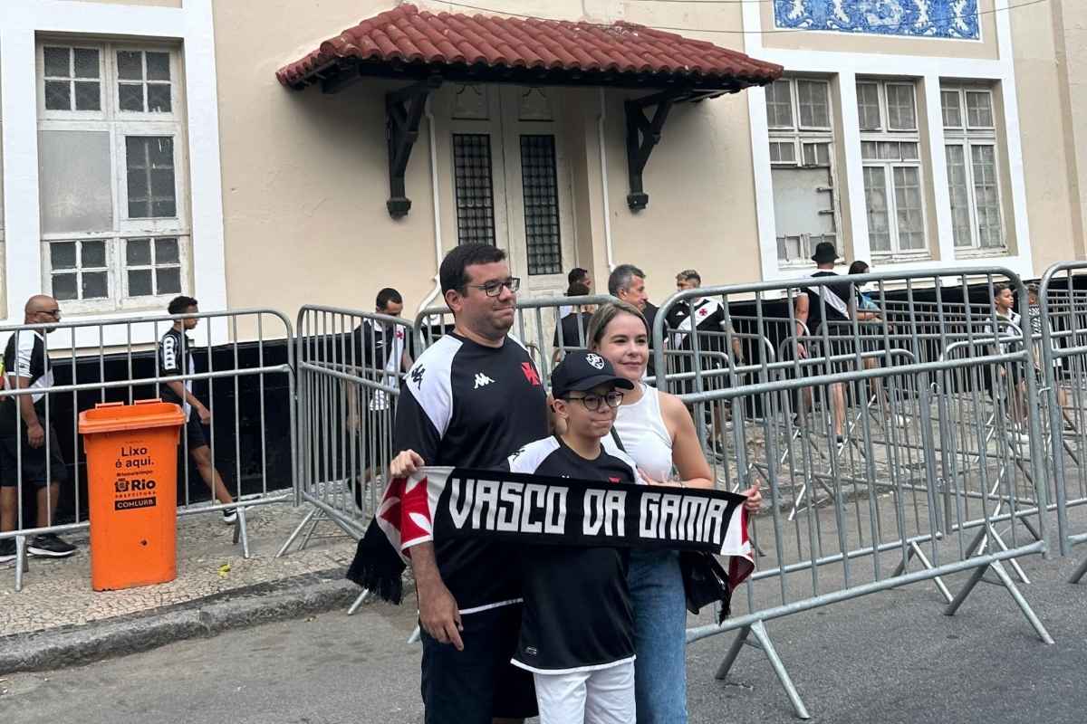 Família de torcedores do Vasco segurando cachecol Vasco da Gama em frente à fachada histórica de São Januário